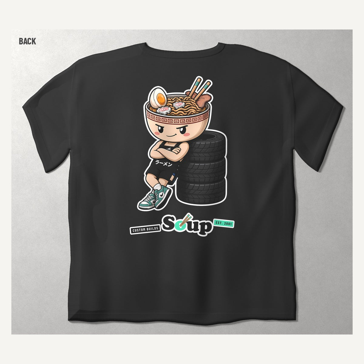 Soup Syndicate Tyre Stack Soupman tee in washed black, back view with Soupman sitting on a tyre stack over the Soup sticker row